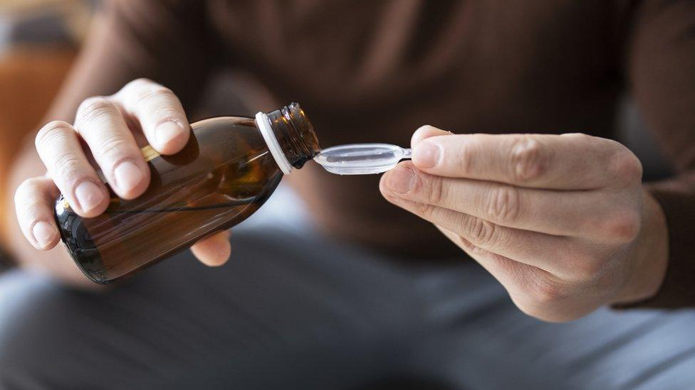 A clinical bottle of prescription cough syrup with codeine sitting on a sterile counter next to a precise dosing syringe
